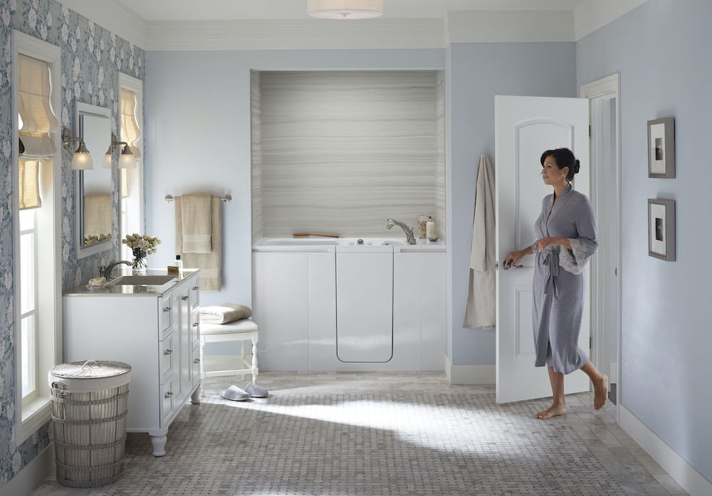 Woman enters bathroom, featuring a KOHLER Walk-In Bath.
