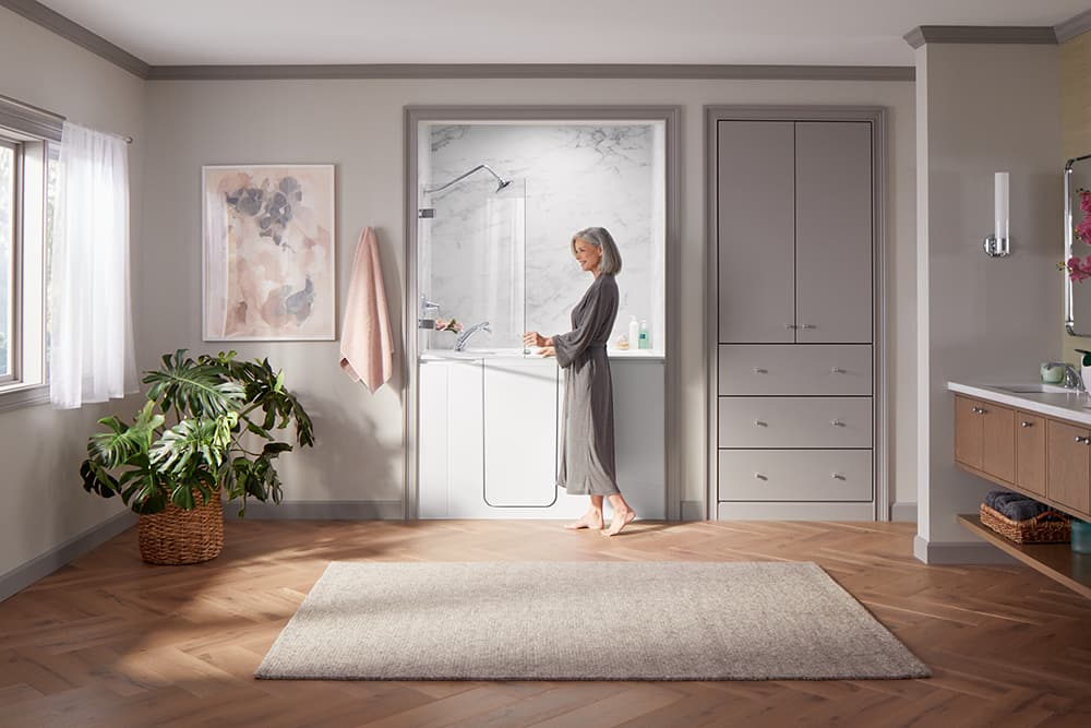 Woman standing in a large bathroom gripping the bath screen of her walk in tub shower package