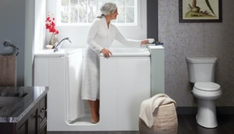 woman in robe easily entering her walk-in bath holding the handrail on rim of bath